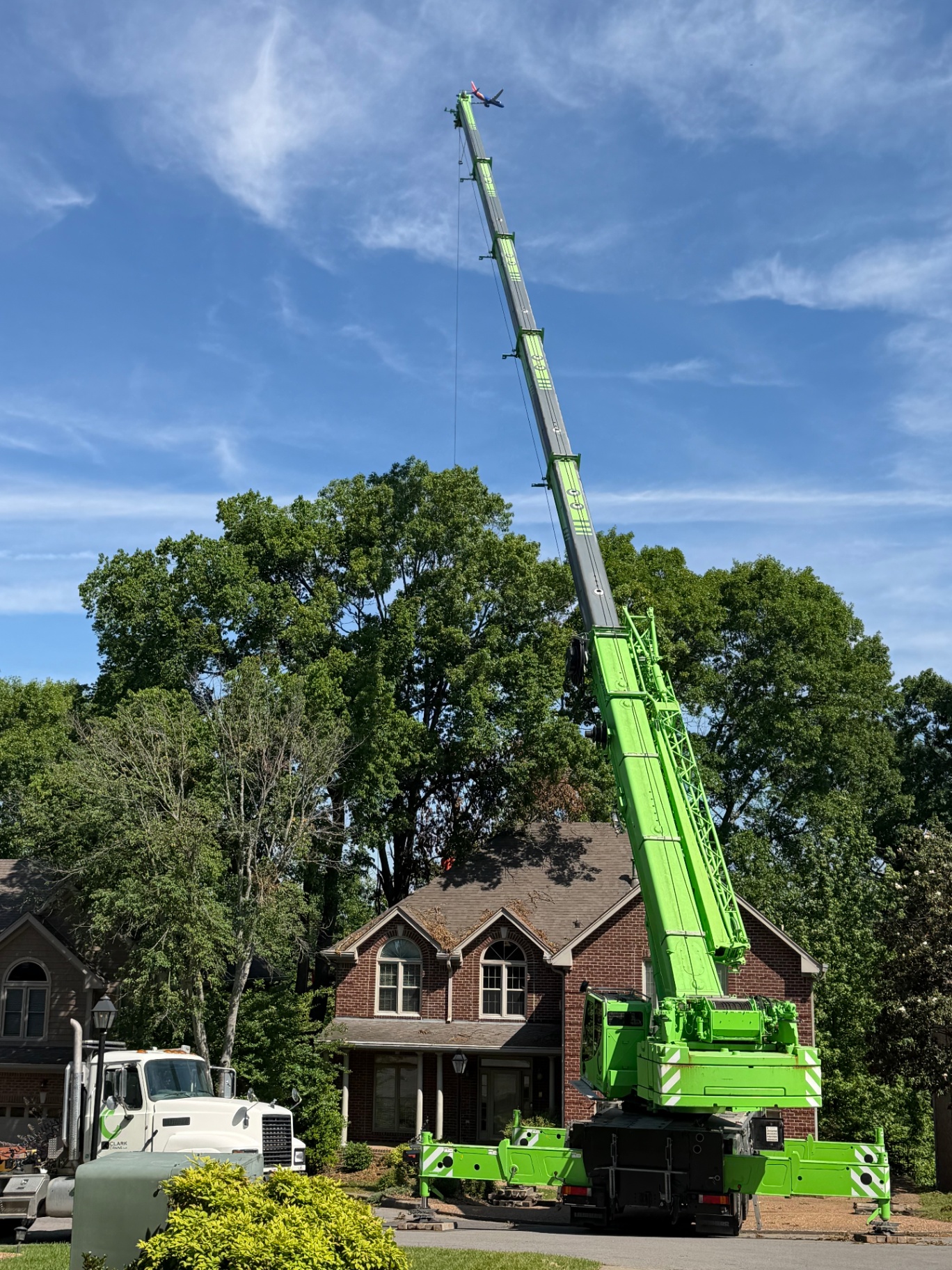 Large green Sennebogen crane positioned at a Nashville brick home for a careful tree removal